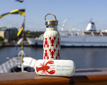 A glasses case and water bottle with lobster designs on the are sitting on the railing of Britannia. 