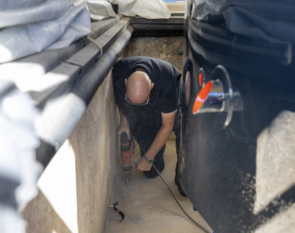 A maintenance man is crouching next to the Royal Barge in it's pond to prepare it for adding a new filtration system. 