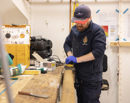 A Maintenance team member holding a sander, removing varnish off of a handrail. 