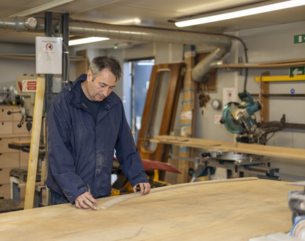 A Maintenance team member making a template on wood. 
