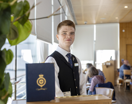 A server is standing at a welcome podium in the Royal Deck Tearoom, ready to welcome visitors. 