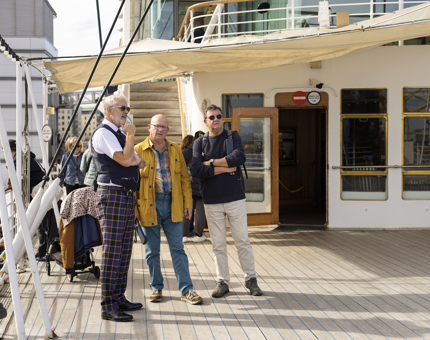 One of Britannia's Visitor Assistants is on the Verandah Deck talking to two visitors in the Port of Leith. 