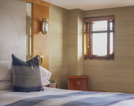 A bed with white sheets and a tartan throw blanket and pillow aboard Fingal in Leith.