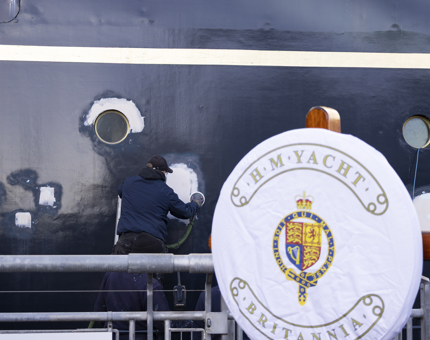 The hull of The Royal Yacht Britannia in the Port of Leith is being sanded by a maintenance man, 