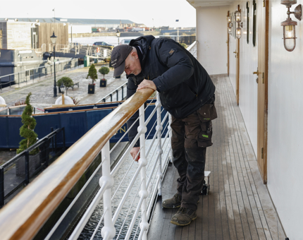 A Maintenance man is leaning over the railings on Fingal's deck to add a coat of paint. 
