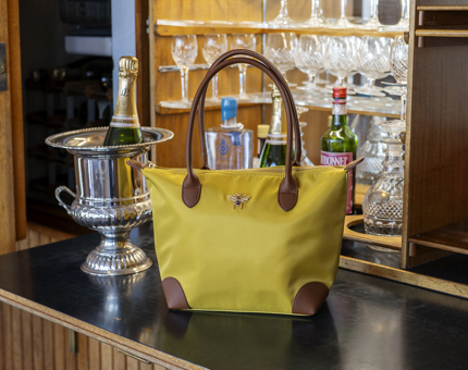 A yellow handbag with a bee detail is sitting on a bar. 
