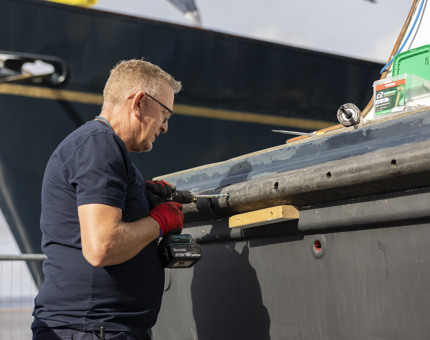 A close up of a Maintenance team member working on the refurbishment of the Admiral's Fast Motor Launch boat. 