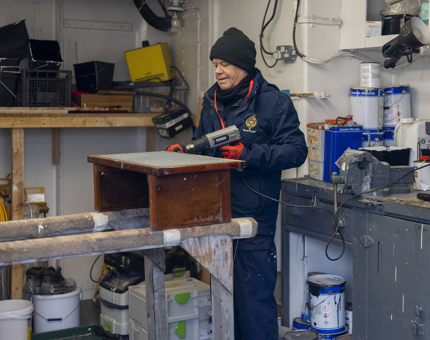 A Maintenance team member is in the workshop using a heat gun to remove varnish from a wooden step. 