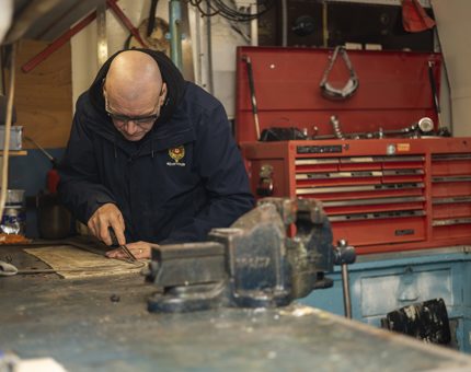 In the workshop, a Maintenance team member is cleaning window surrounds from the Royal Barge. 