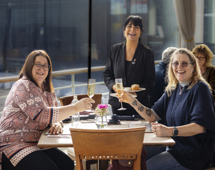 Two ladies are sitting at table being served champagne and scones by a waiter in the Royal Deck Tearoom. 