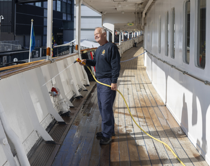 A maintenance man is on the deck, holding a hose, spraying down the side of the deck. 