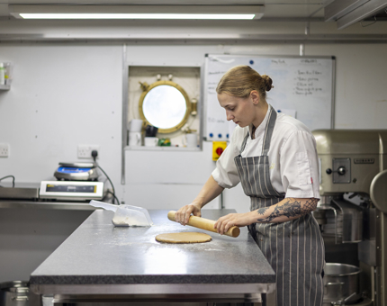 A Chef in the Galley is holding a rolling pin to roll out dough.