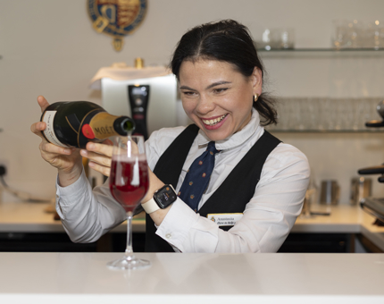 A Hospitality Server is pouring Champagne into a glass to make a Kir Royale cocktail.