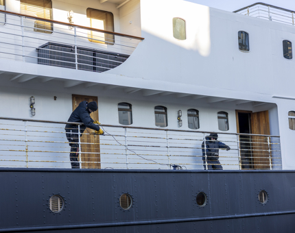 Two maintenance team members aboard Fingal removing paint from the railings. 