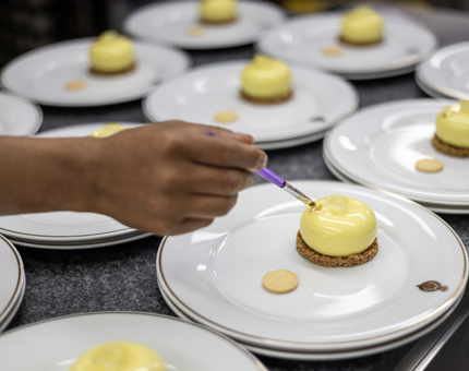 A hand is placing edible gold leaf on small cheesecakes. 