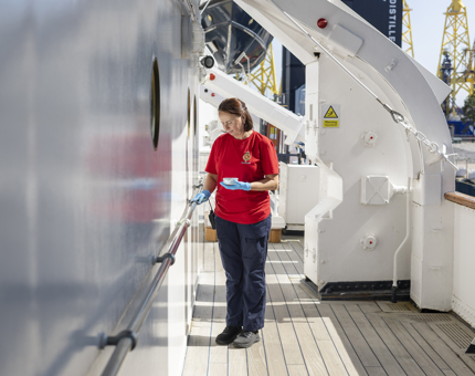 A housekeeper is polishing a brass handrail on the decks of Britannia. 
