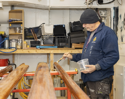 A man is applying varnish to wooden handrails, The Royal Yacht Britannia.
