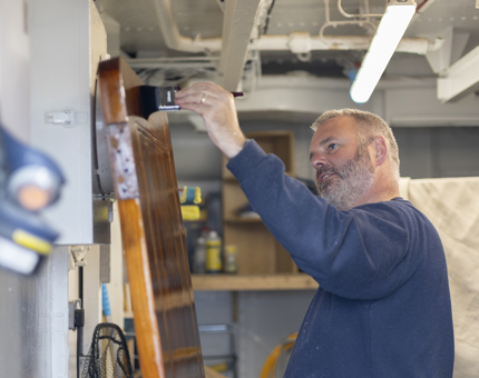 A Maintenance man holding a paintbrush, applying varnish to a door. 