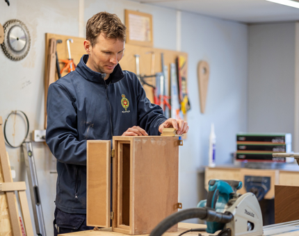 A Maintenance team member sanding a wooden box for the Bridge. 