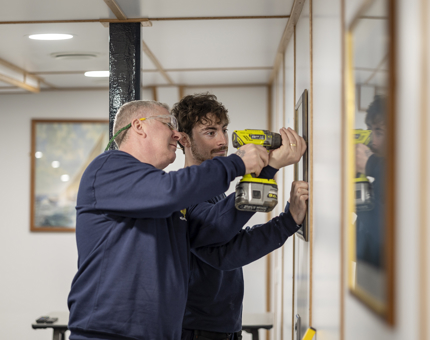 Facilities Officers Paul and Scott hanging pictures in Training Room.