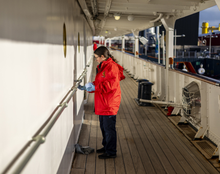 A woman in a red jacket is polishing handrails on Britannia. 