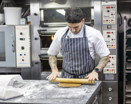 A Chef in the onboard Galley rolling out dough with a rolling pin. 
