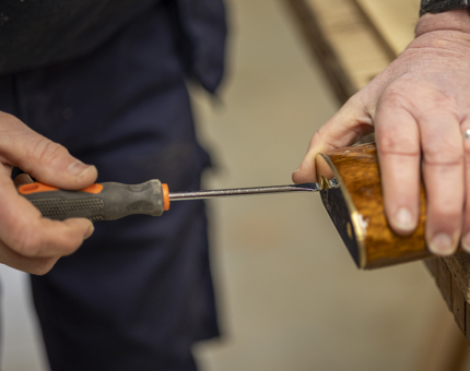 A close up of a hand holding a screwdriver attaching brass ends to a handrail. 
