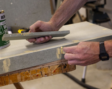 A close up of hands applying wood filler to a shelf. 