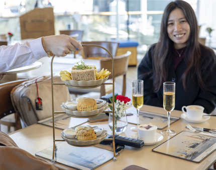 A visitor is sitting at a table in the Royal Deck Tearoom aboard Britannia, they are being served a cream tea. 