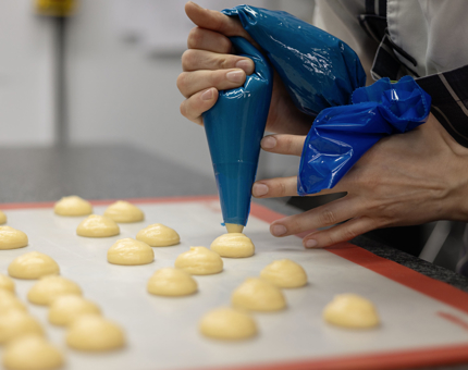 A close up of a Chef in Britannia's Galley holding a blue piping bag, piping choux buns onto a tray.