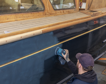 Maintenance team member holding a sander, removing paint from the Royal Barge. 