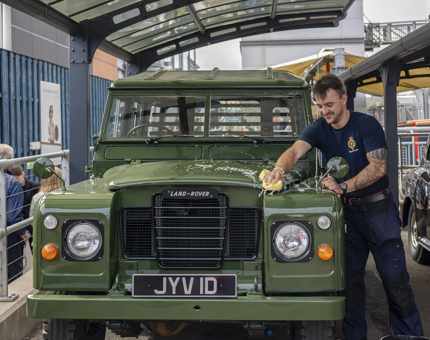 A facilities Officer is using a sponge to clean a green Land-Rover. 