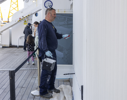 A maintenance man is painting the Starboard side of the ship white. 
