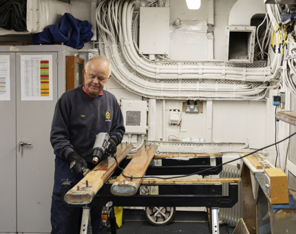 A maintenance team member is using a heat gun, stripping varnish from handrails. 