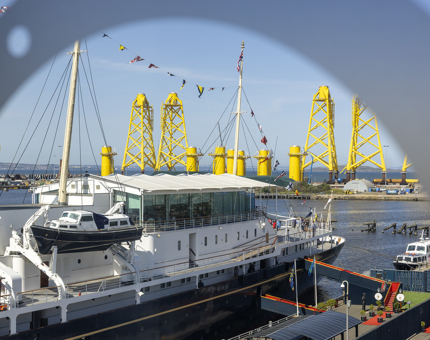 A view of Britannia from the Visitor Centre window. There are yellow pilons in the background in the Port of Leith. 