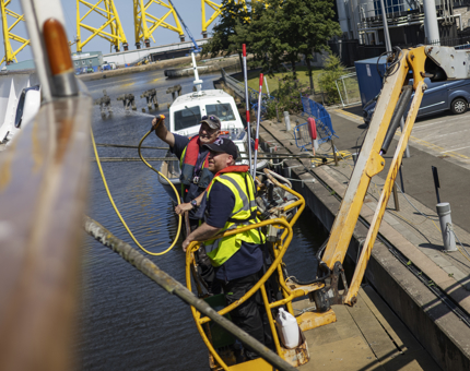 Two maintenance men are on a yellow cherry picker hosing down the side of Britannia in Leith. 