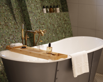 A freestanding bathtub aboard Fingal Hotel. The wall behind it has small green tiles. 
