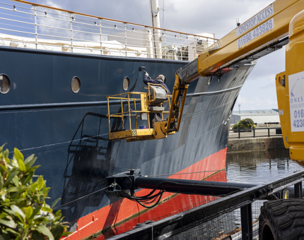 A yellow cherry picker has a Maintenance team member in it, who is painting the side of Fingal Hotel in Leith. 