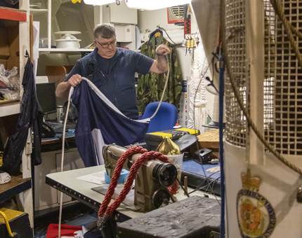 A maintenance man is in a workshop holding dress flags to be raised above Britannia. 