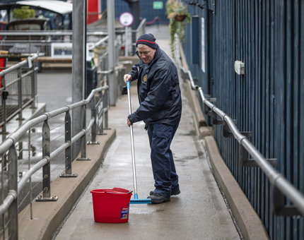 A Facilities Officer scrubbing the walkway on the quayside with a broom, 