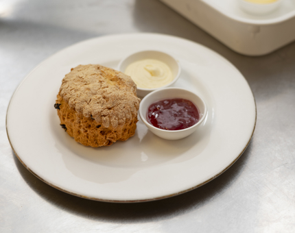 A white plate has a fruit scone with dishes of cream and jam next to it. 