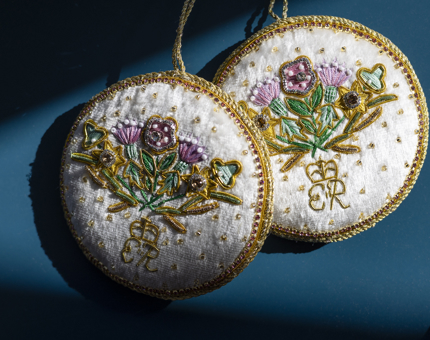 Two round decorations with embroidered flowers and the initials ER. 