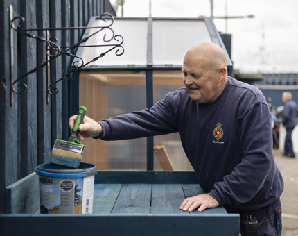 A Facilities Officer painting a set of potting shelves with blue paint. 