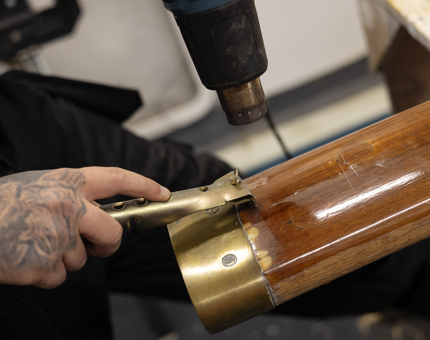 A close up of a hand holding a heat gun and scraper to remove varnish from a heat gun. 