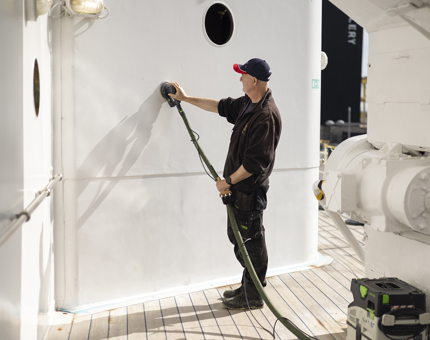 A Maintenance team member is sanding a white wall on the port side of Britannia in Edinburgh.