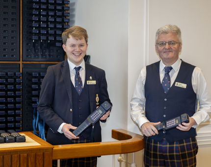 Two Visitor Assistants standing with audio guide handsets to give to guests visiting The Royal Yacht Britannia in Leith. 