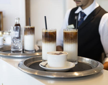 Trays of drinks, such as iced lattes and coffees are on trays, ready to be served in the Tearoom aboard Britannia. 