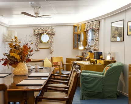The Admiral's Day Cabin, there is a dining table, green armchair and a writing desk. 