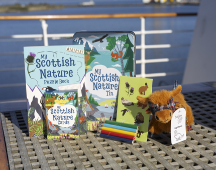 Items such as an activity book, cards, coloured pencils and a Highland cow plush, from a 'My Scottish Nature ' tin activity set. 