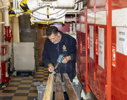 A man from Maintenance is removing varnish from handrails in the workshop.